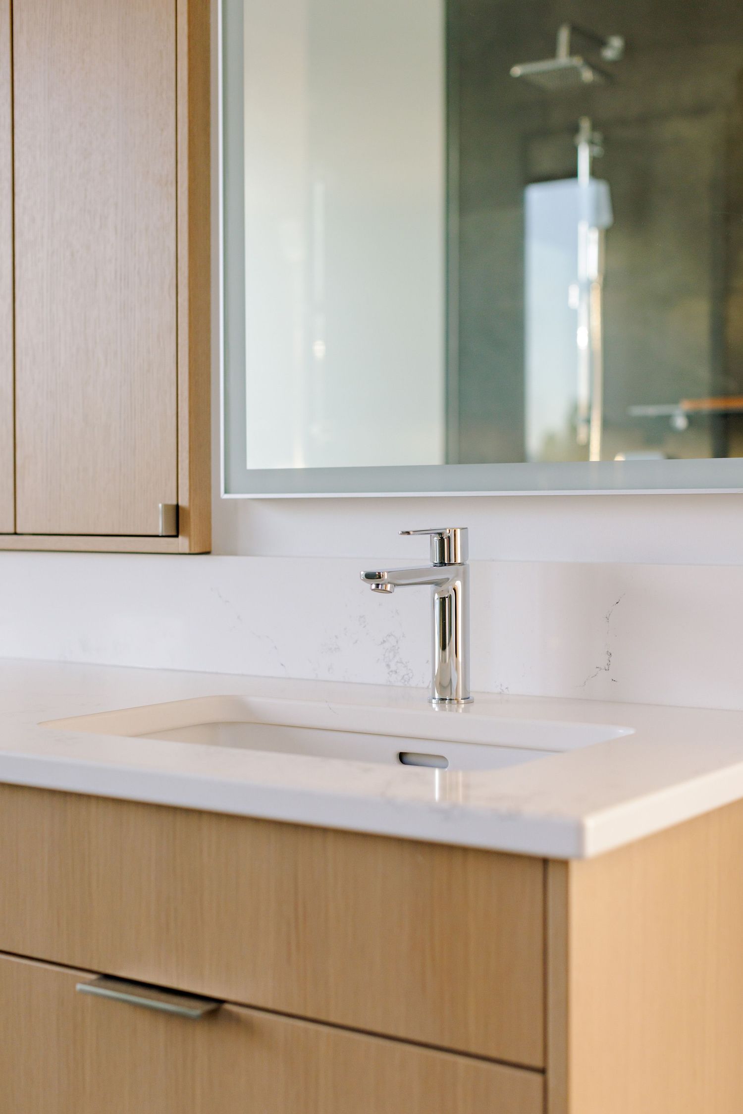 Modern bathroom vanity with light wood cabinets and a sleek chrome faucet mounted on white quartz countertop.
