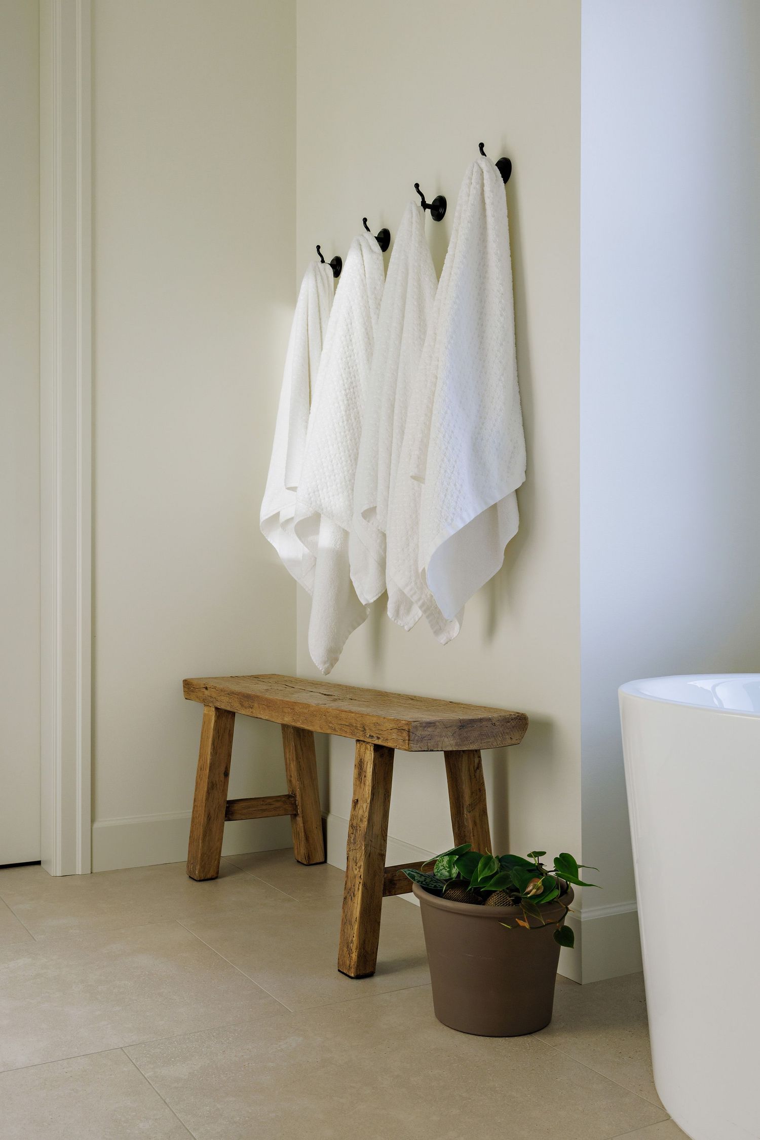 White towels hanging on rustic wooden benches against a cream wall with a potted plant on the floor.