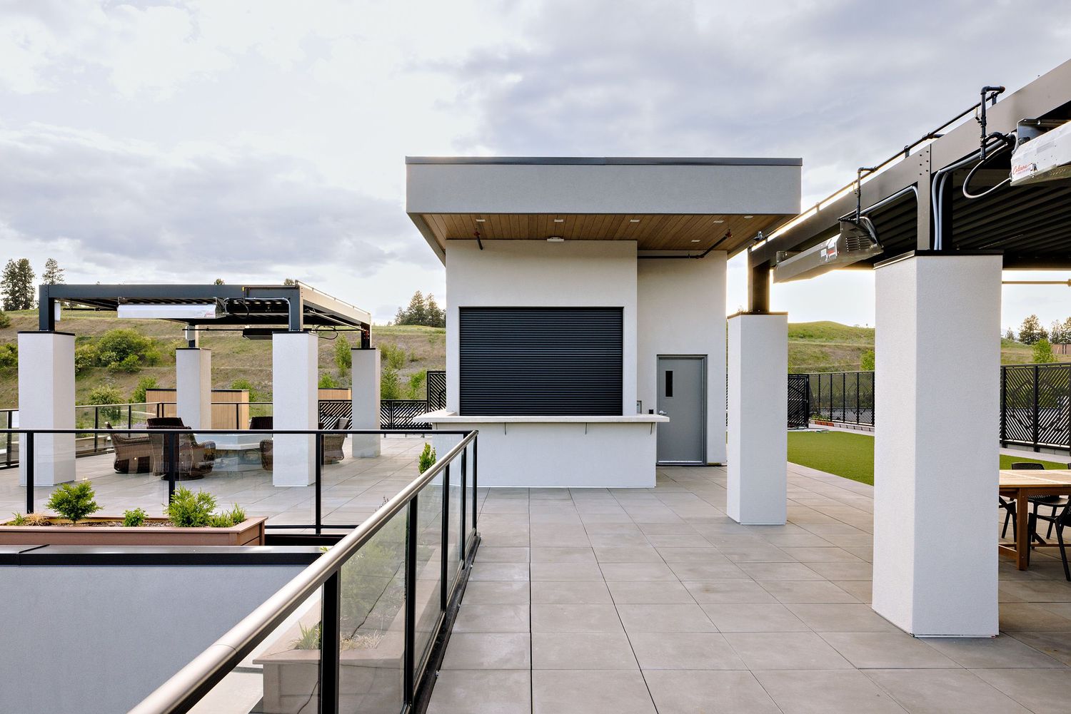 Modern outdoor rooftop patio with white pillars, black railings, and a built-in entertainment area on a cloudy day.