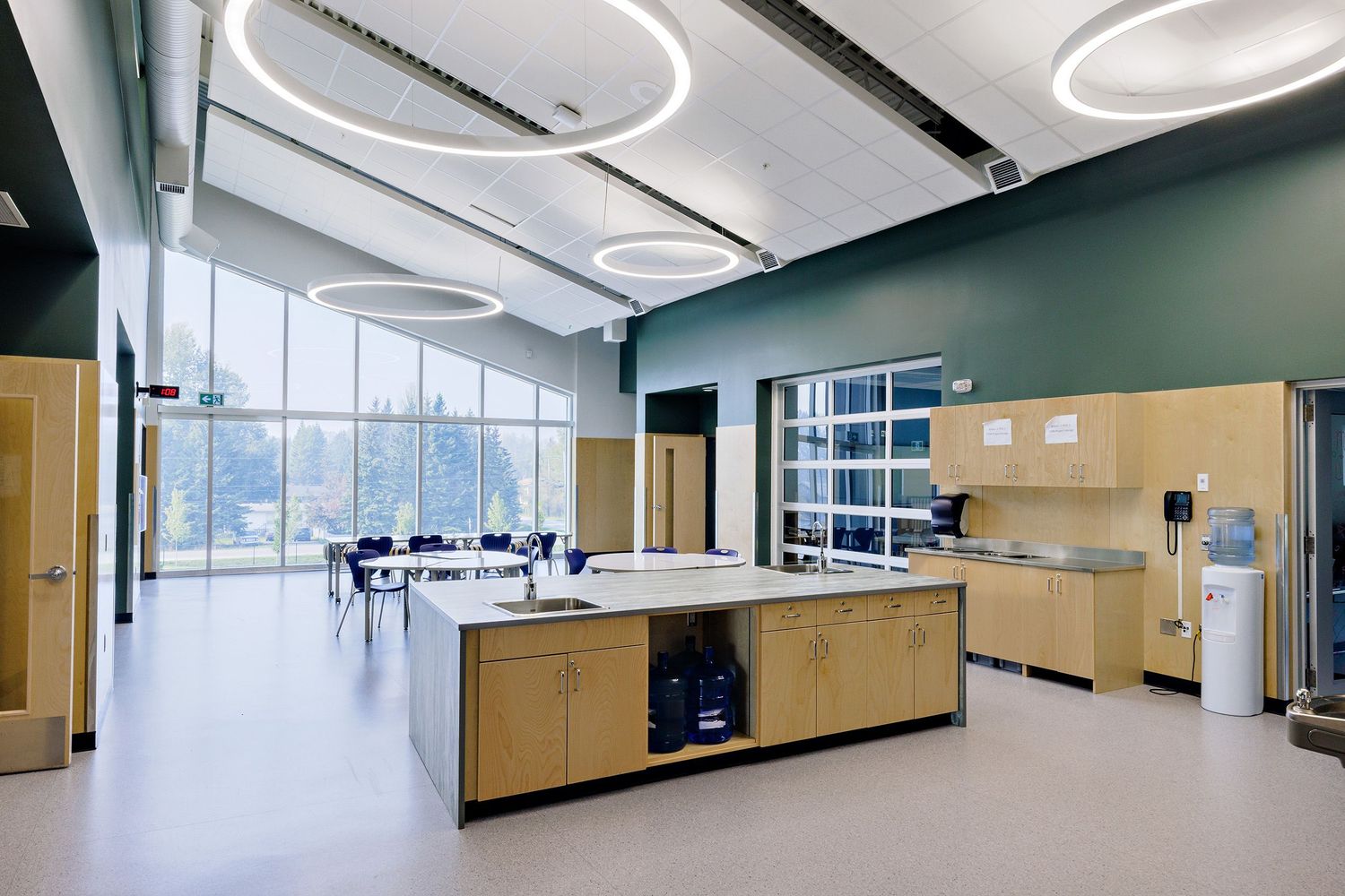Bright modern classroom interior with light wood cabinets, green walls and large windows offering natural lighting.