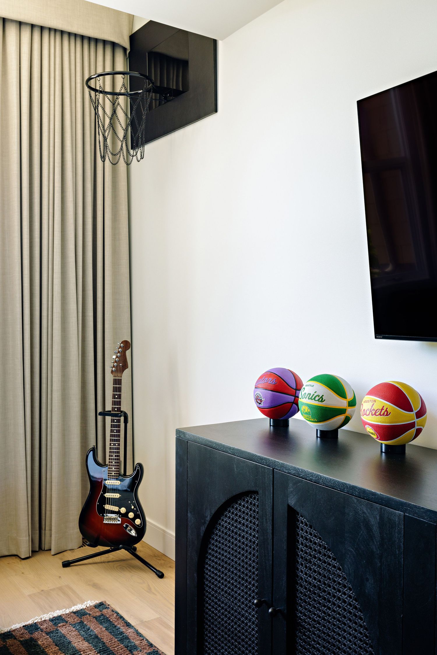 Entertainment area with basketball hoop, electric guitar, and colorful basketballs on black cabinet.