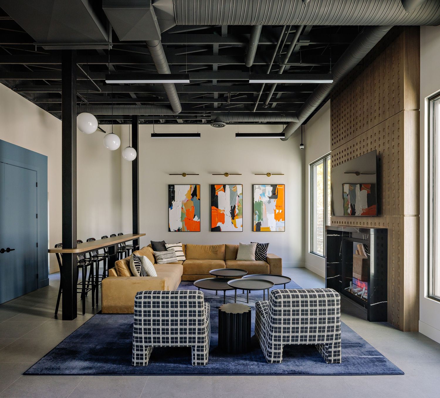 Modern office space with exposed ceiling, geometric patterned seating areas, and industrial-style lighting fixtures.