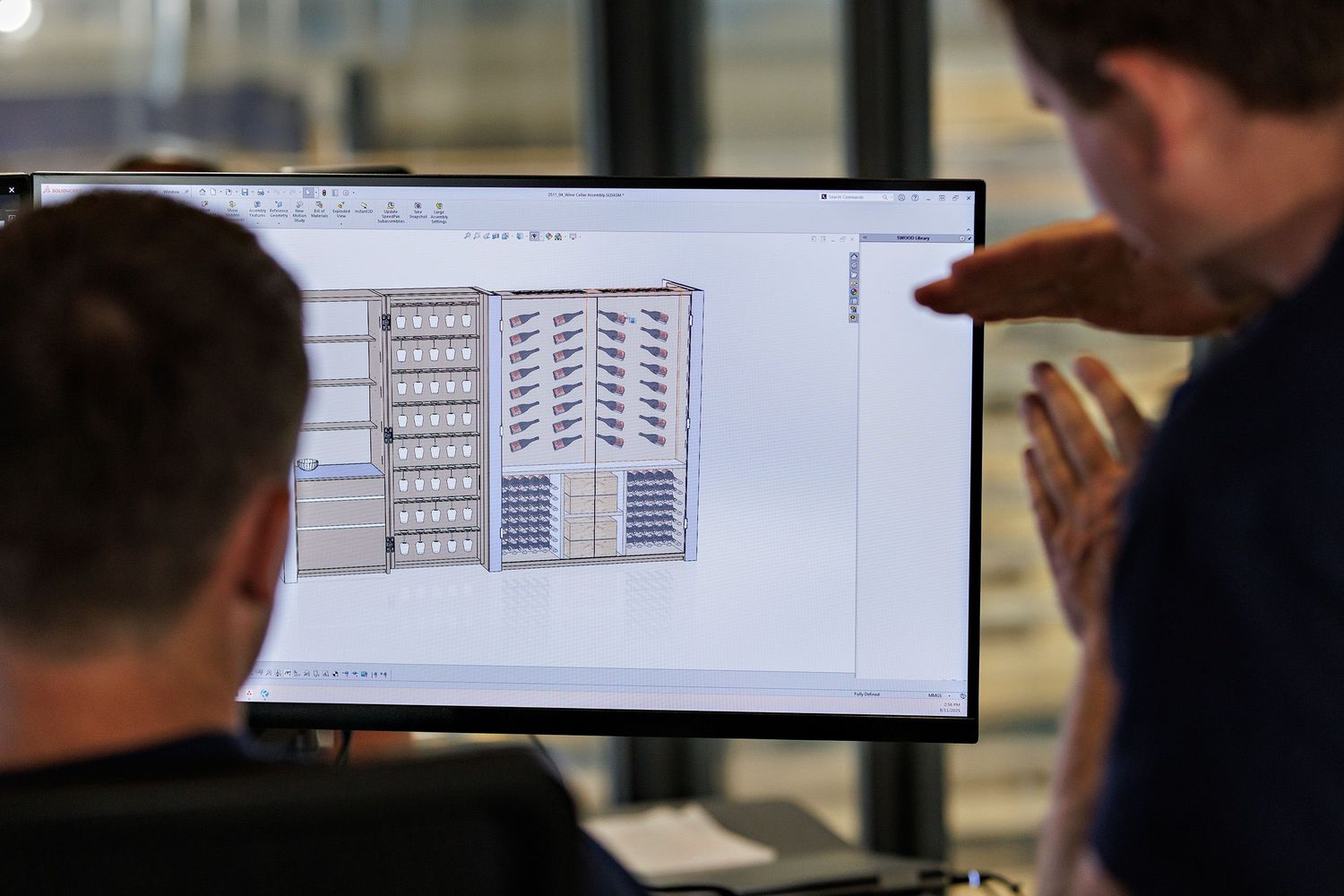 Technical drawings and blueprints displayed on computer screens in an office setting.