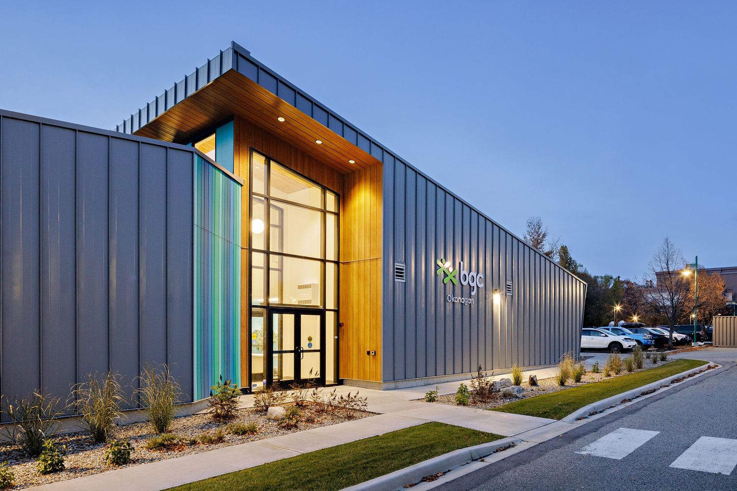 Contemporary industrial building exterior with metal siding and illuminated entrance at dusk.