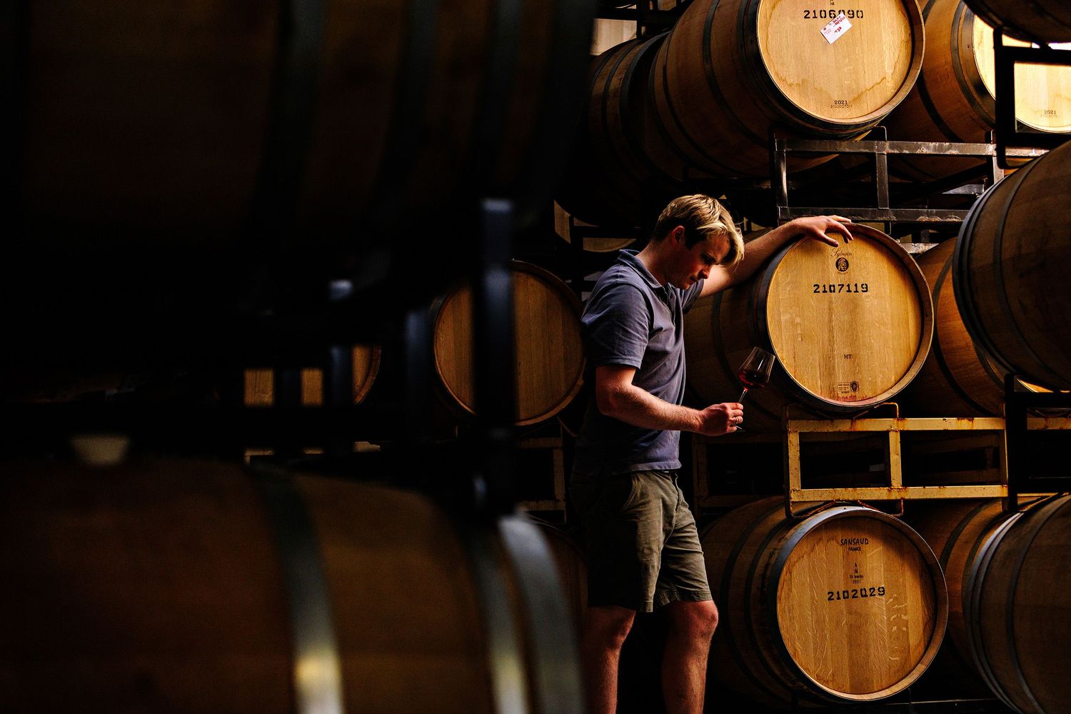 A person checks wine barrels in a dimly lit cellar at a winery during the aging process.