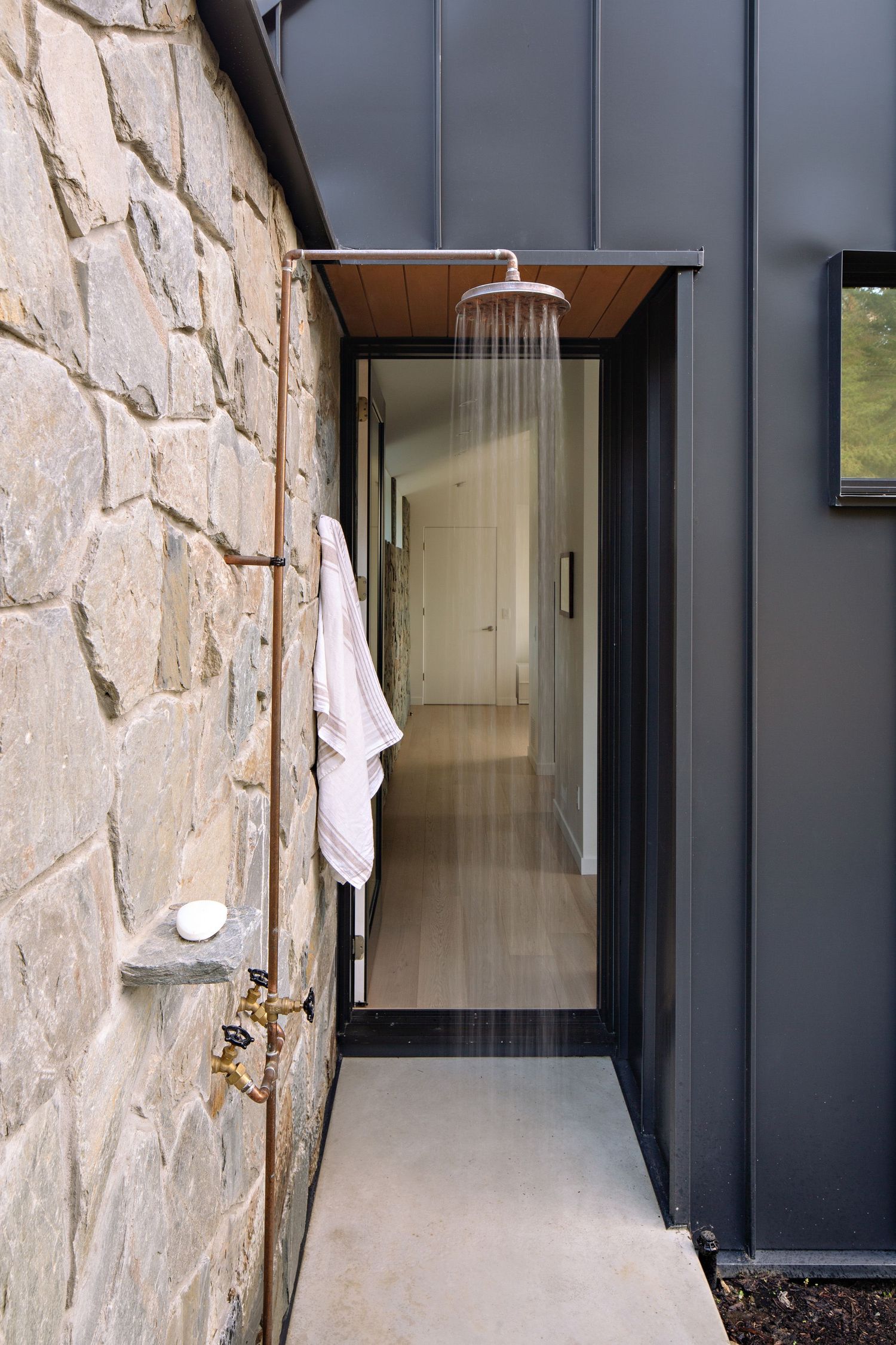 Modern outdoor shower enclosure with stone wall and black metal siding features a rainfall showerhead and minimalist design.
