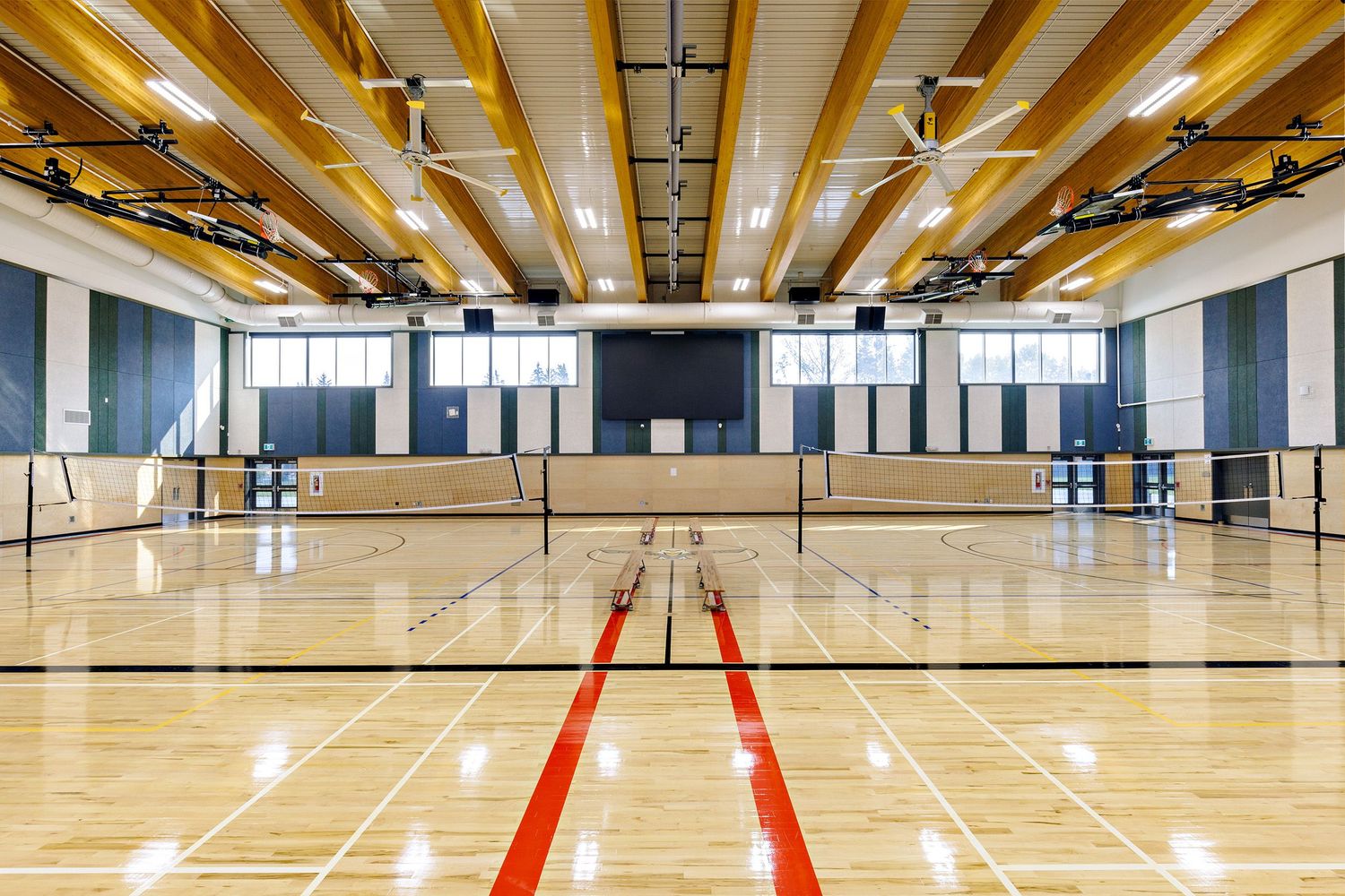 Indoor gymnasium with hardwood floors, volleyball nets, and yellow beams on the ceiling.
