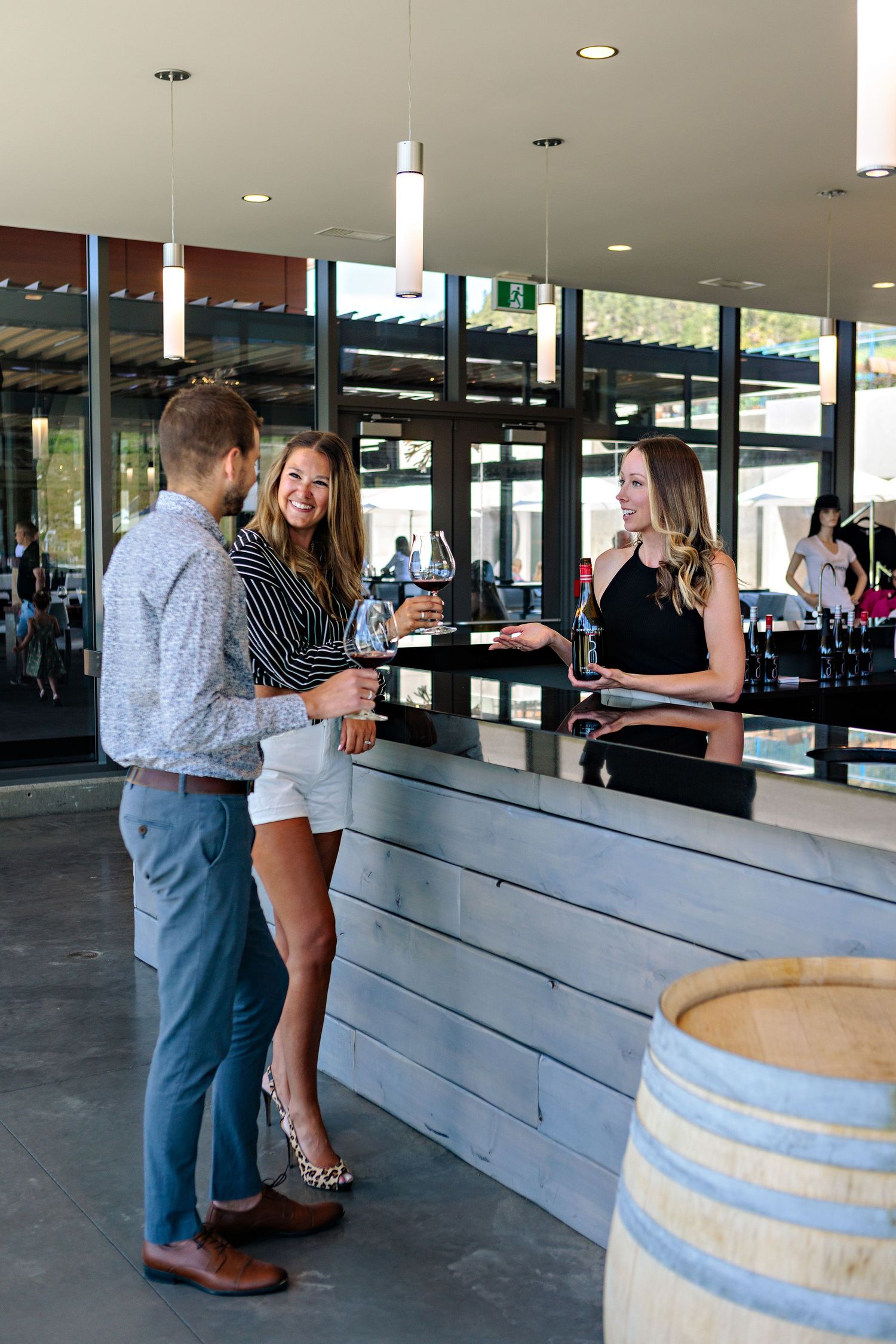 Guests enjoy wine tasting at a modern winery bar with wooden barrels and pendant lighting.