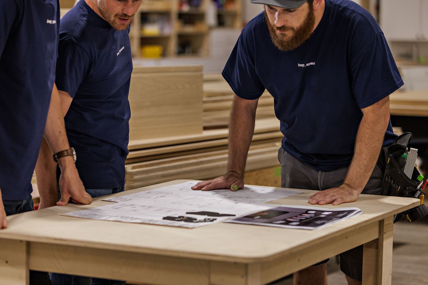Workers in navy uniforms review documents on a workbench.