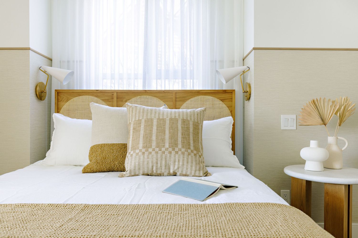 Contemporary bedroom with white bedding, beige accents, and natural light streaming through windows.