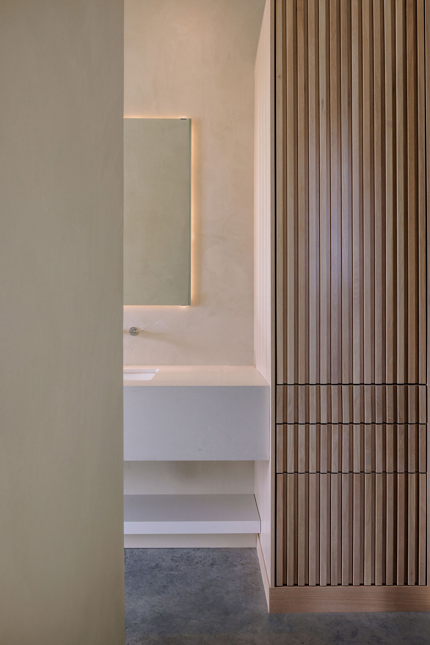Minimalist bathroom interior with wooden slat wall feature and floating vanity with backlit mirror.