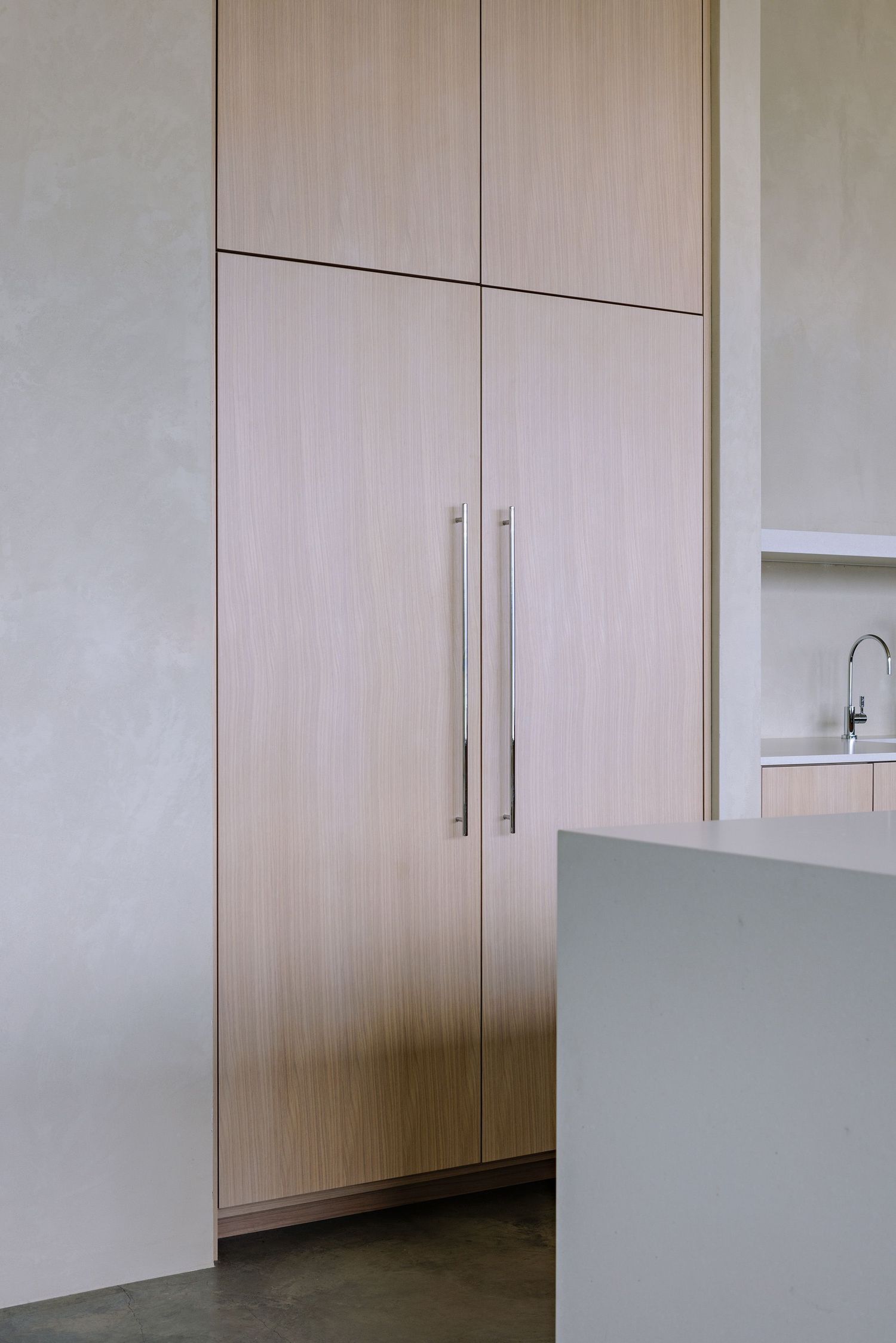 Sleek built-in floor-to-ceiling cabinet with light wood finish and long metal handles in a modern kitchen space.