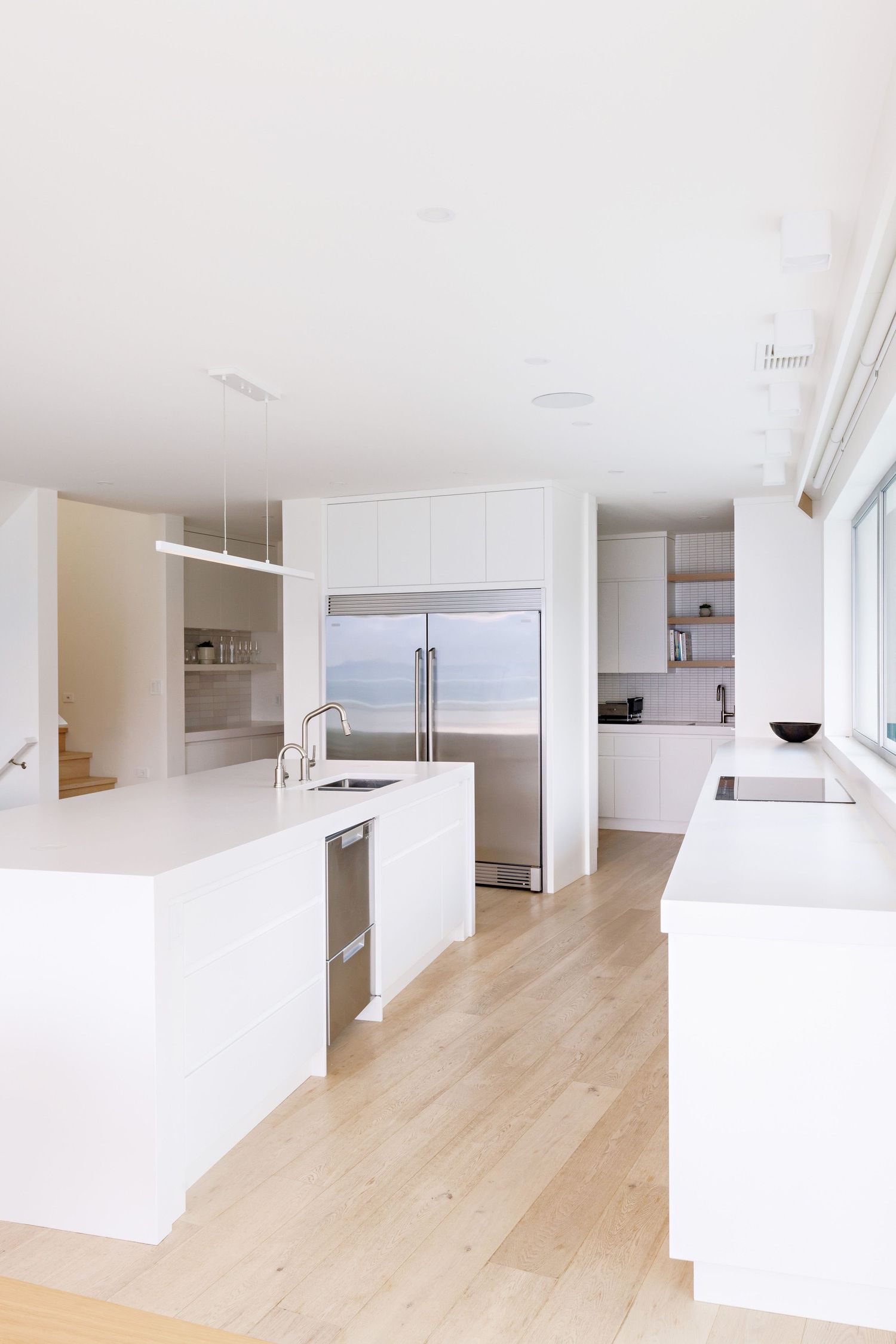 Sleek white contemporary kitchen with light wood floors and stainless steel appliances.