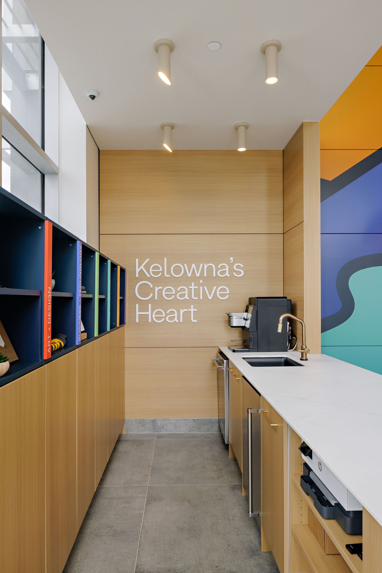 Modern office kitchenette with wooden cabinets and 'Kelowna's Creative Heart' text displays a minimalist design aesthetic.
