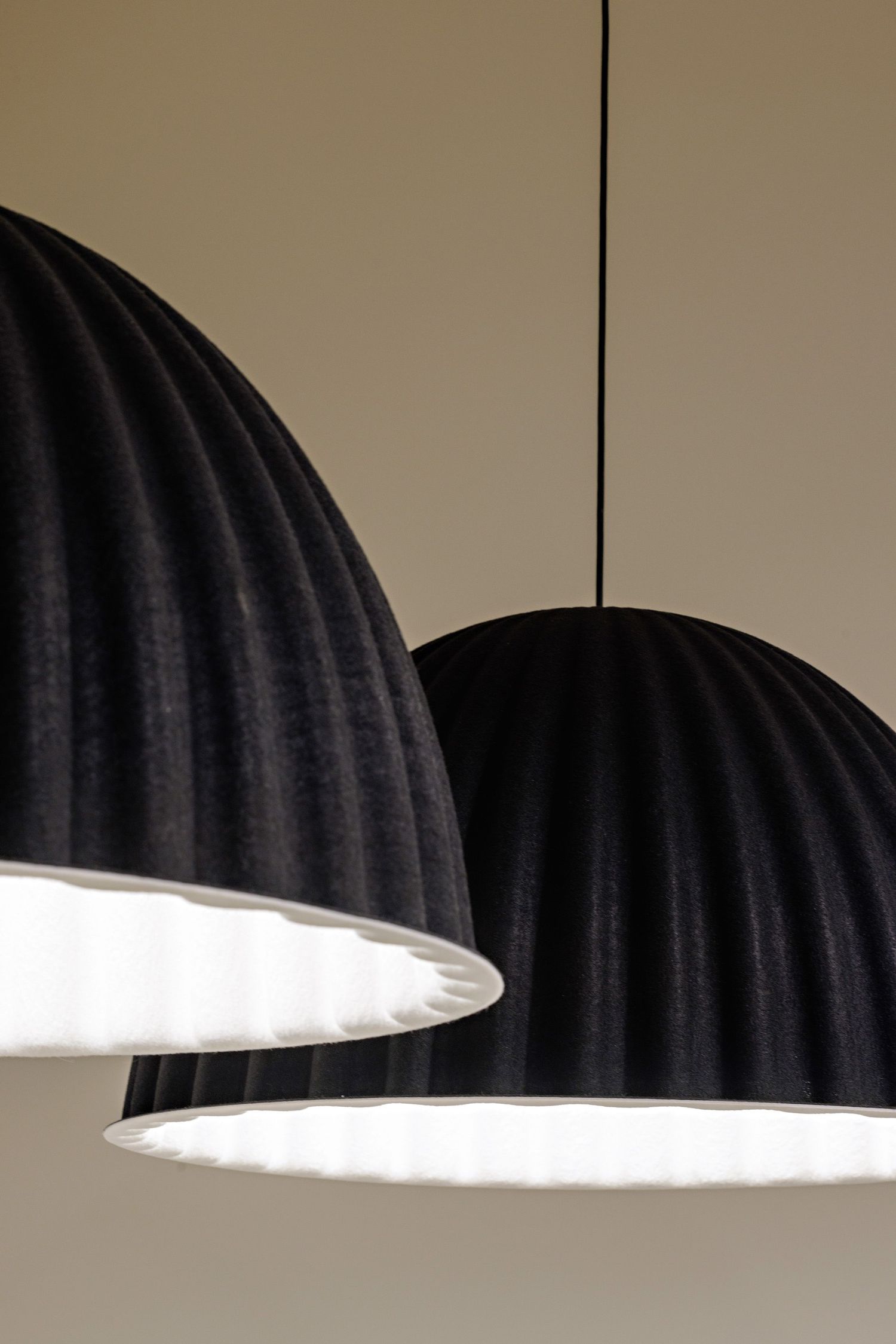 Two black dome-shaped pendant light fixtures with ribbed texture and bright white interiors hang against a beige wall.