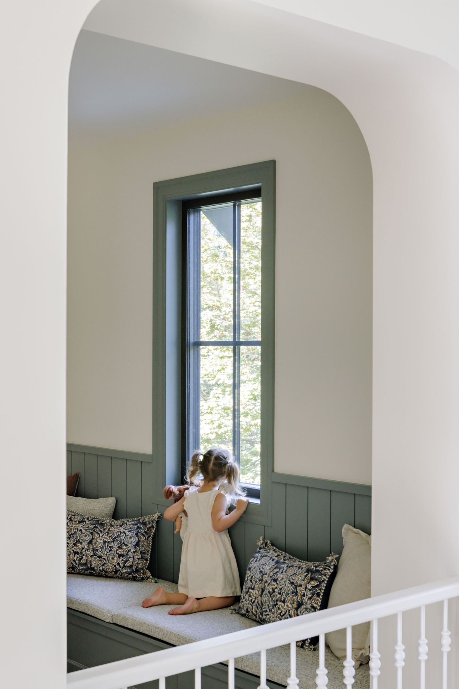 Cozy built-in window seat nook with white walls, green wainscoting, and floral pillows creates a charming reading corner.