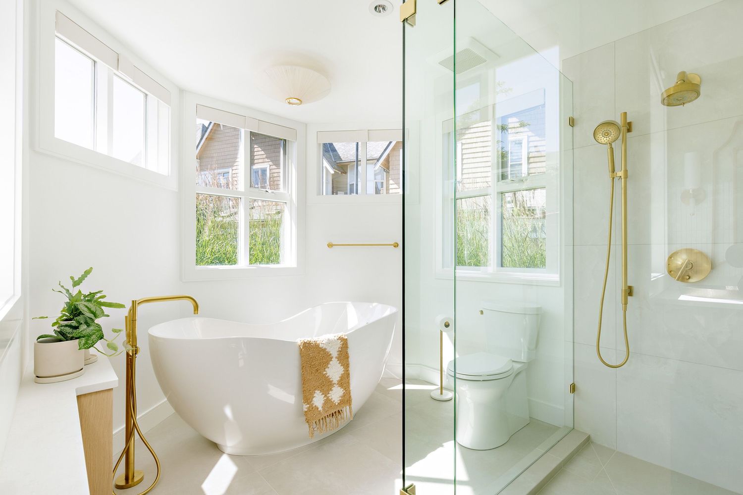 Luxurious white bathroom featuring freestanding tub, glass shower enclosure, and gold fixtures.
