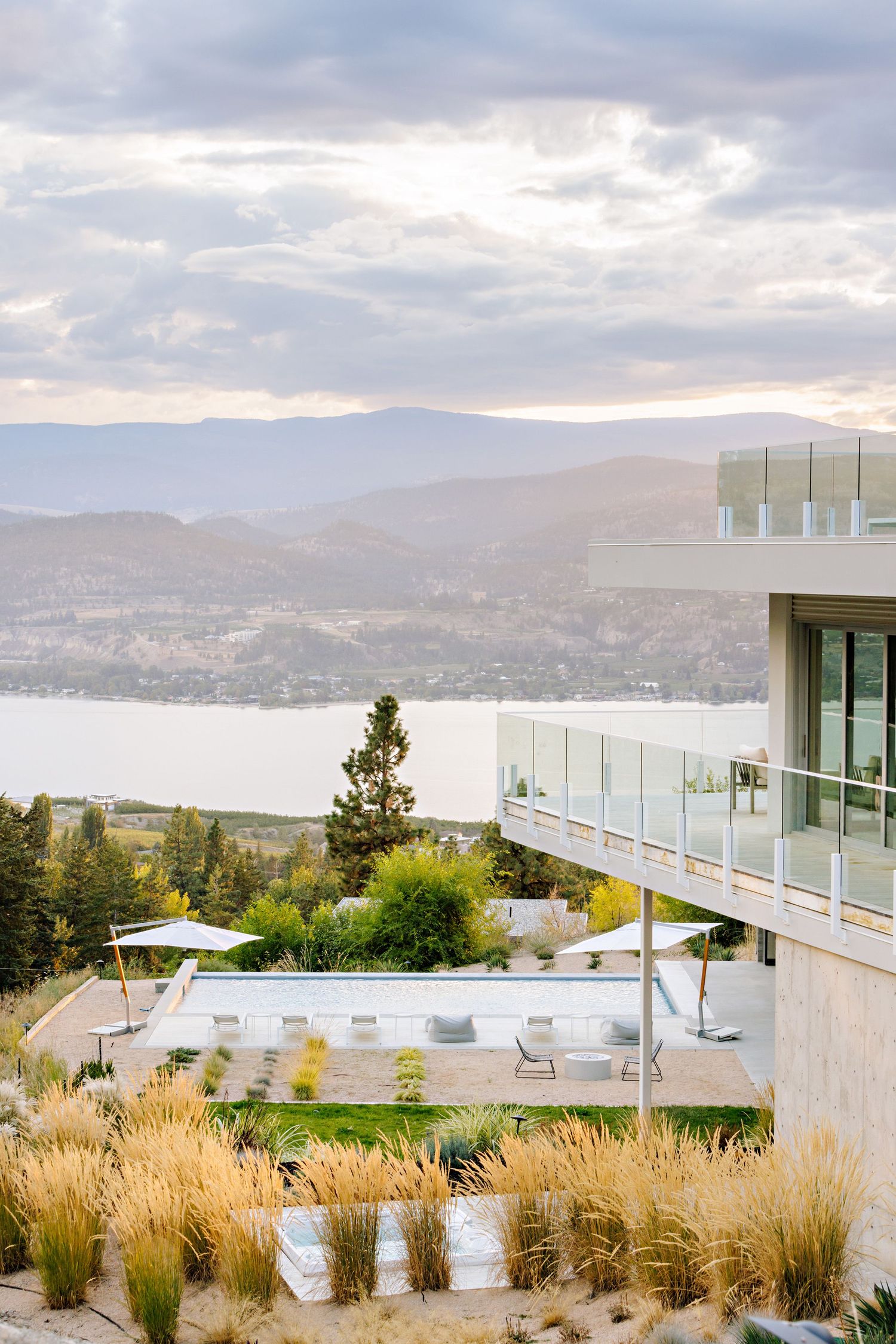 Modern hillside property with outdoor lounge area overlooking a stunning mountain lake vista.