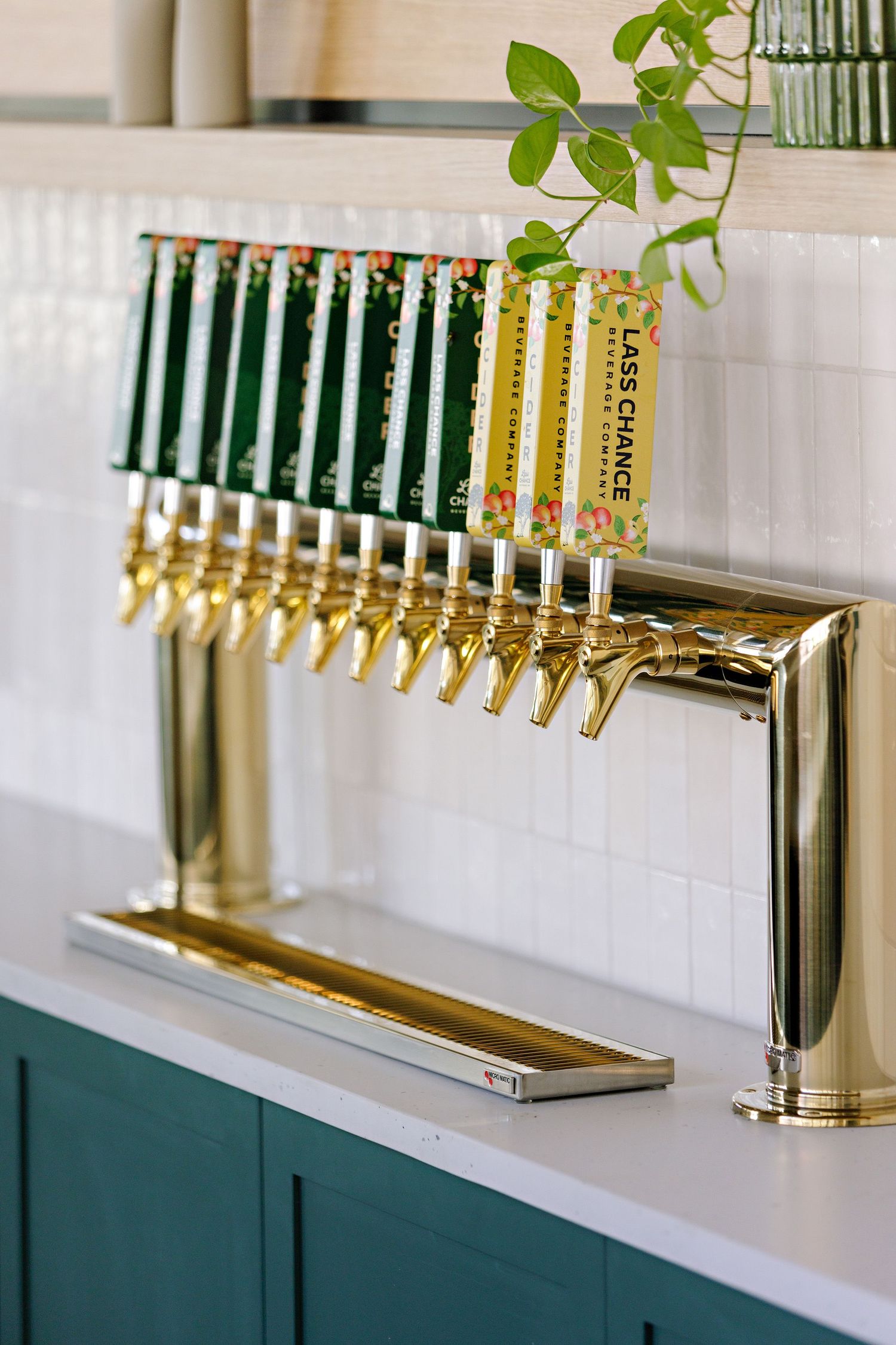 Modern beer tap system with brass handles and green and yellow tap markers mounted on white countertop with green cabinets.