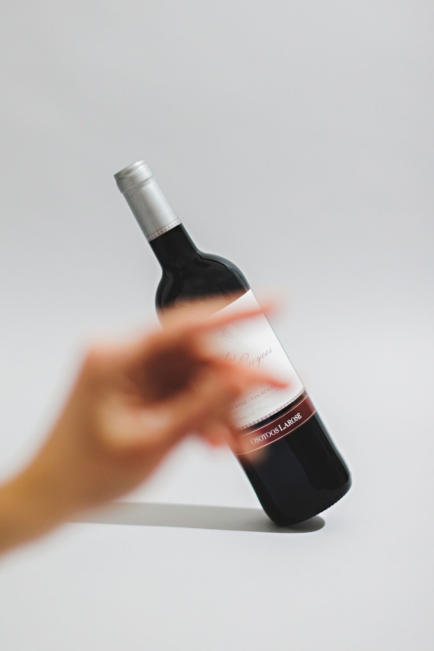 Motion blur shot of a hand reaching for a bottle of red wine against white background.