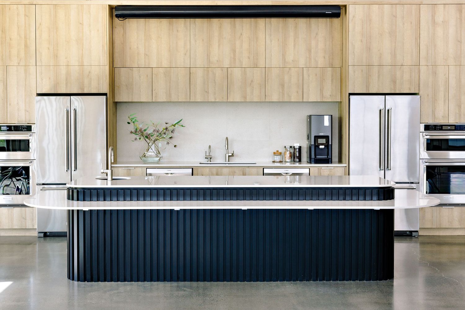 Modern minimalist kitchen featuring a navy blue ribbed island with white countertop and dual refrigerators in light wood cabinetry.