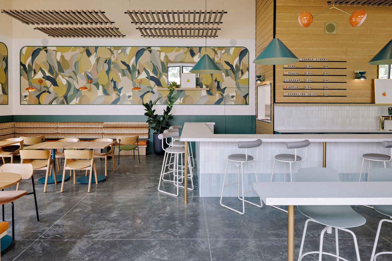 Modern restaurant interior featuring concrete floors, white bar seating, pendant lights, and a colorful floral wall mural.