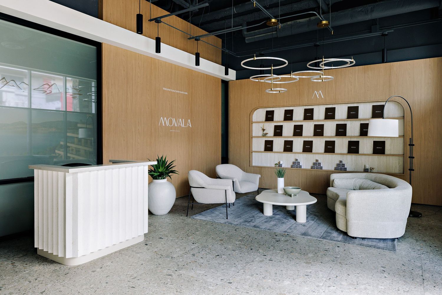 Modern office reception area with light wood walls, white circular pendant lights, and contemporary white lounge furniture.