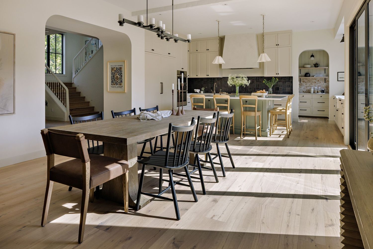 Bright modern dining room interior with white painted wood floors and black Windsor chairs along a rustic wooden table.
