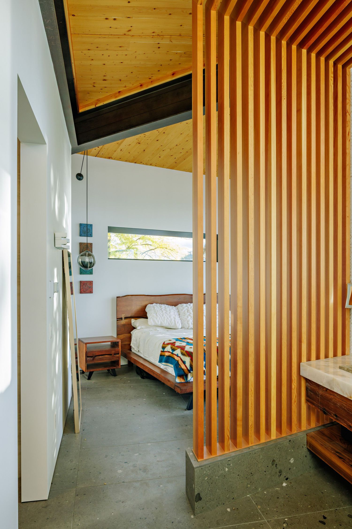 Modern bedroom interior with wooden slat divider and sloped ceiling features natural pine wood accents and minimalist design.