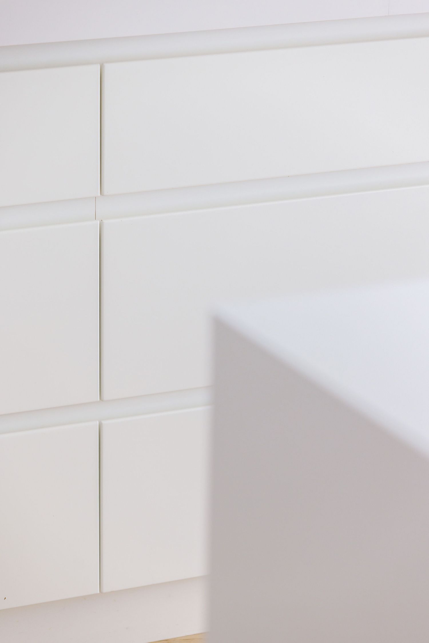 Close-up detail of minimalist white cabinet panels creating clean geometric lines and shadows.