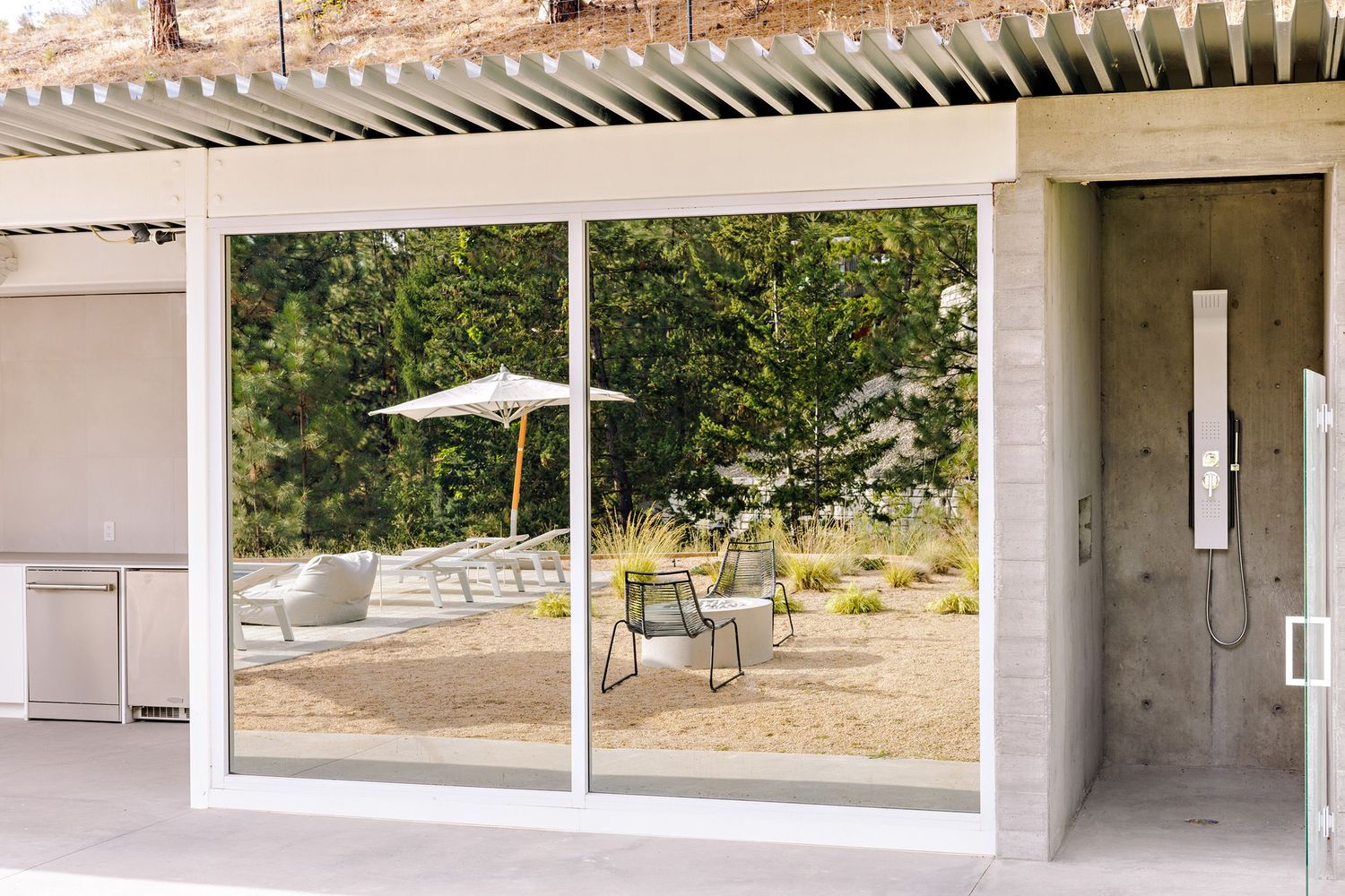 Reflective glass sliding doors mirror an outdoor patio with umbrella and chairs under a modern pergola structure.
