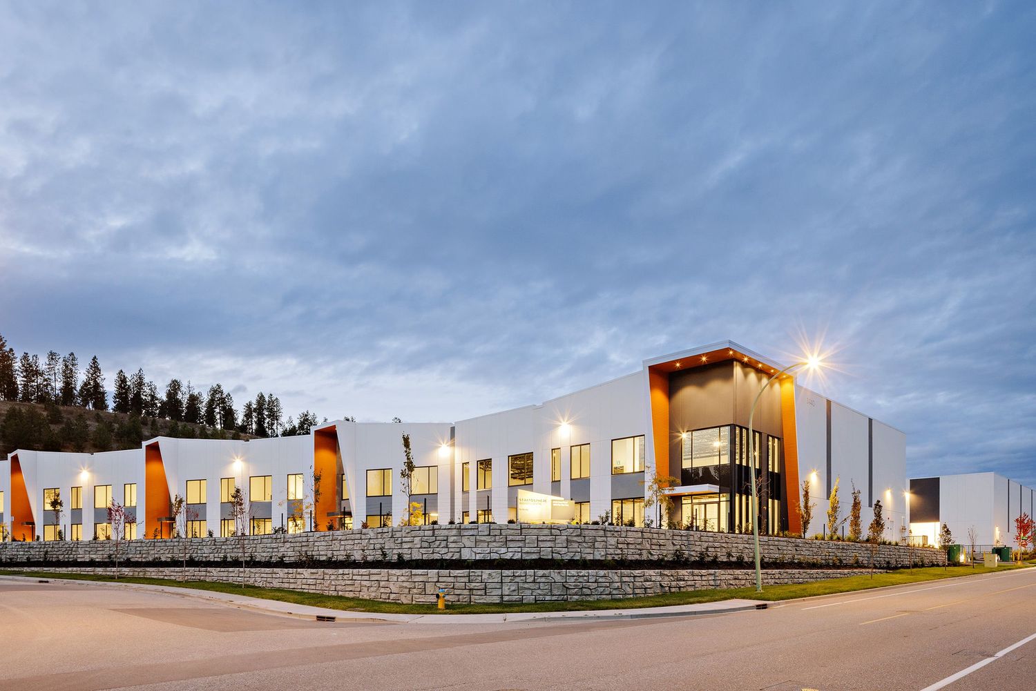 Modern retail shopping center with white exterior walls and orange accents under dramatic cloudy sky at dusk.