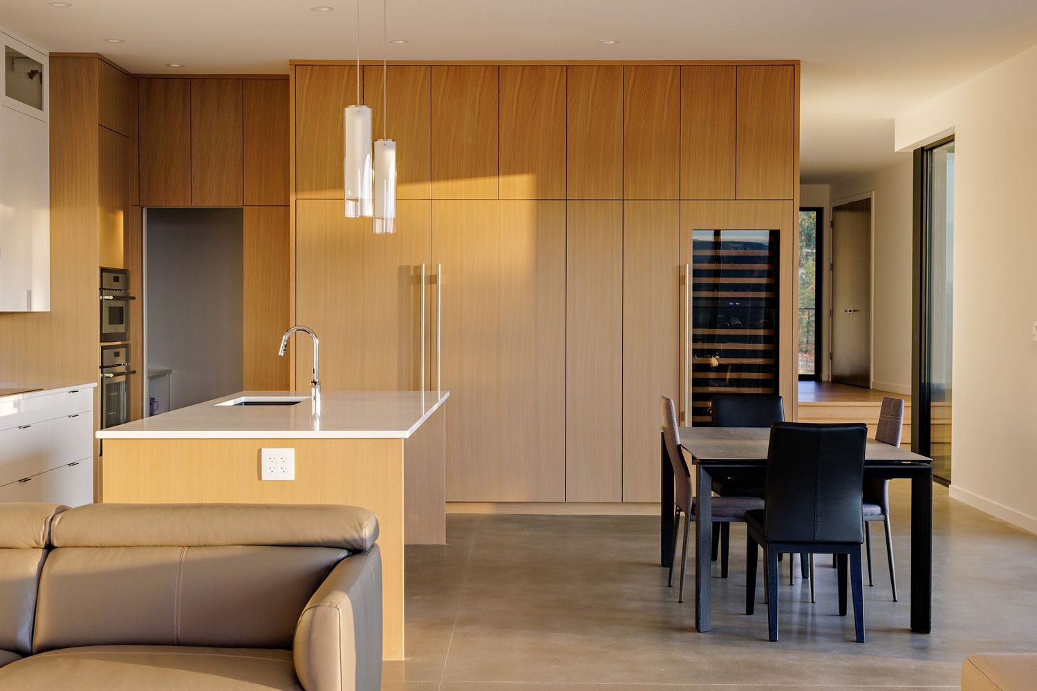 Modern minimalist kitchen with wood paneling, pendant lights, and integrated appliances features a sleek dining area.