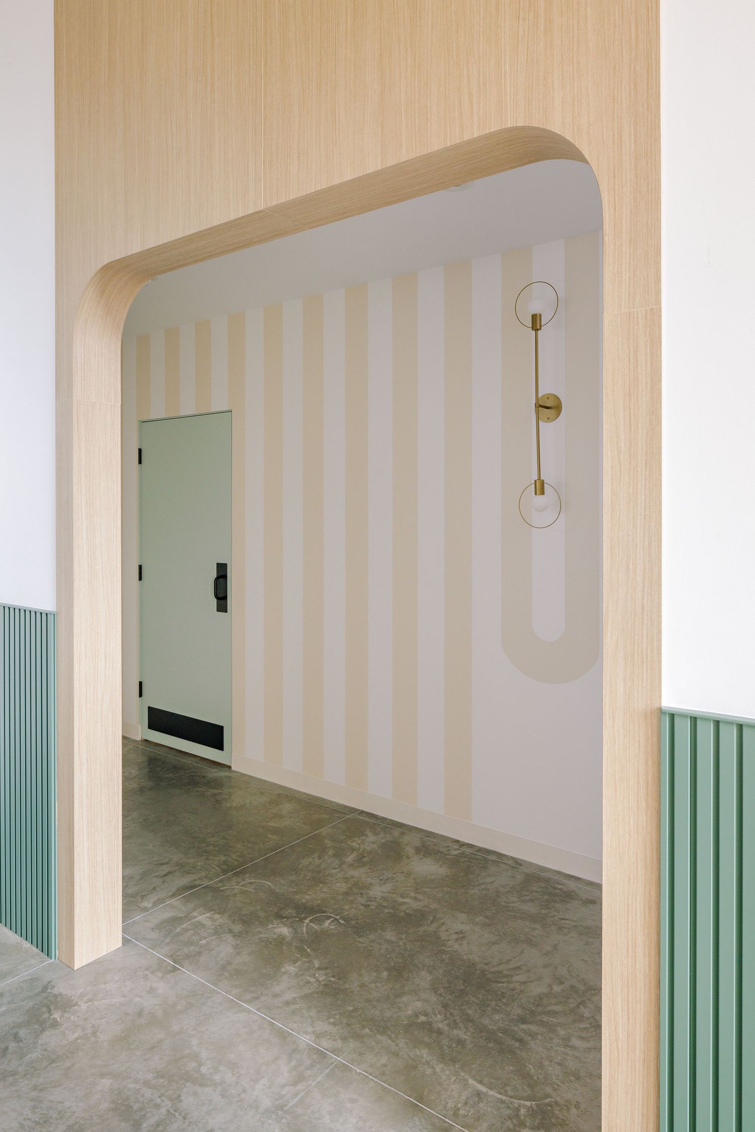 Minimalist hallway with striped wallpaper, arched doorway, and modern sconce lighting fixtures.