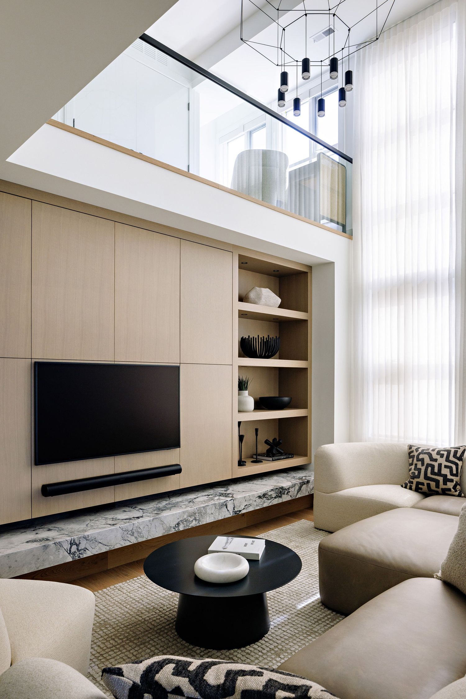 Modern living room with high ceiling, built-in media wall, and blue pendant lights hanging from above.
