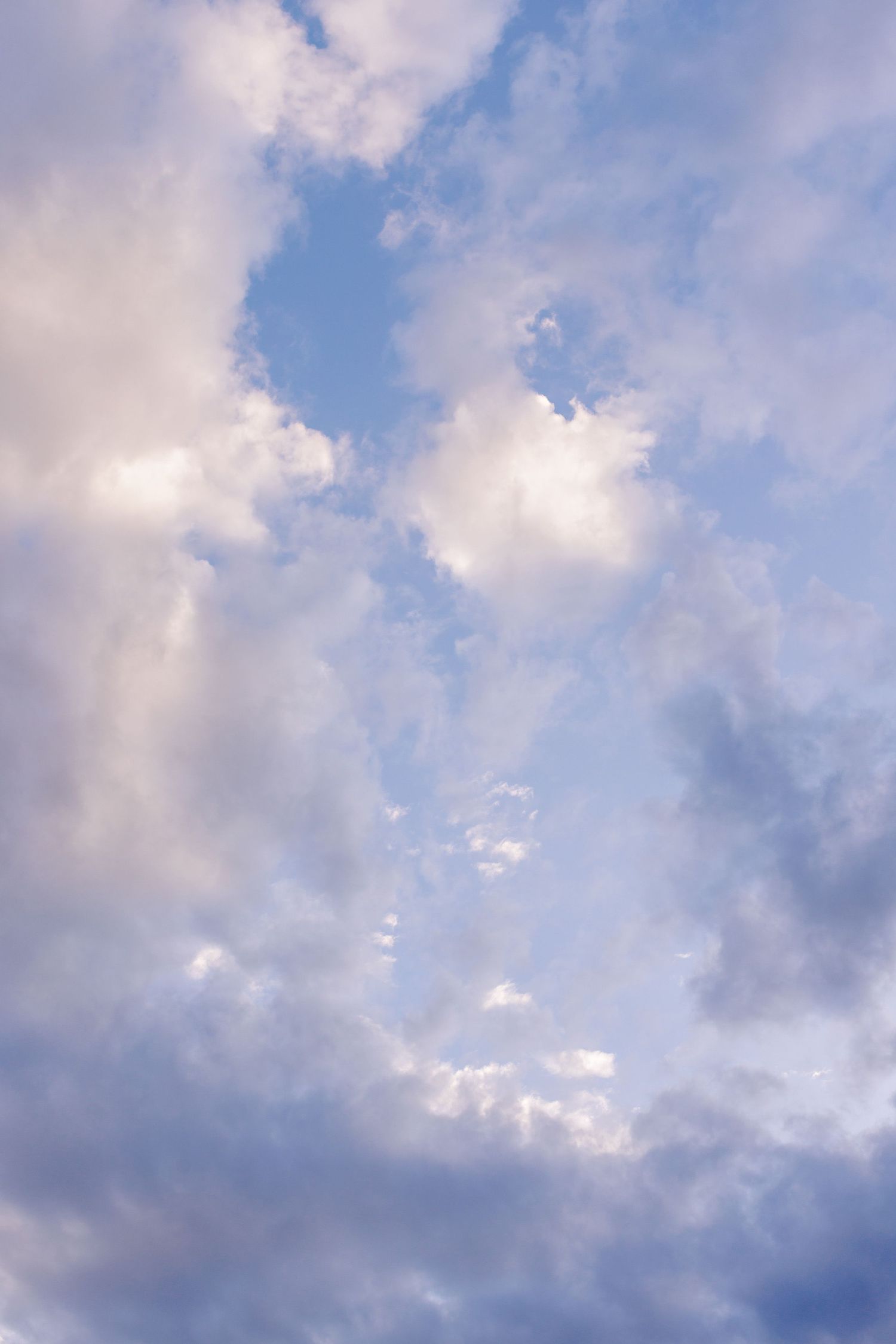 Dramatic purple and white clouds drift across a vibrant blue sky during golden hour.