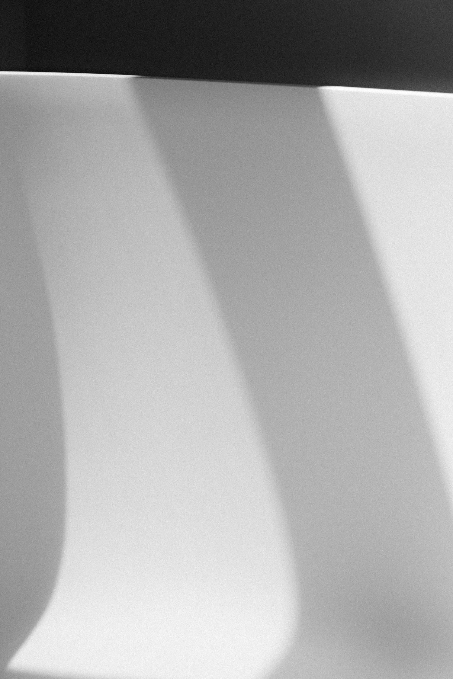 Dramatic shadows cast diagonal lines across white surface in black and white composition.