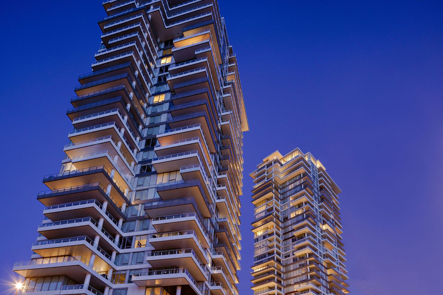 Modern luxury high-rise apartment buildings with illuminated balconies against a twilight blue sky.