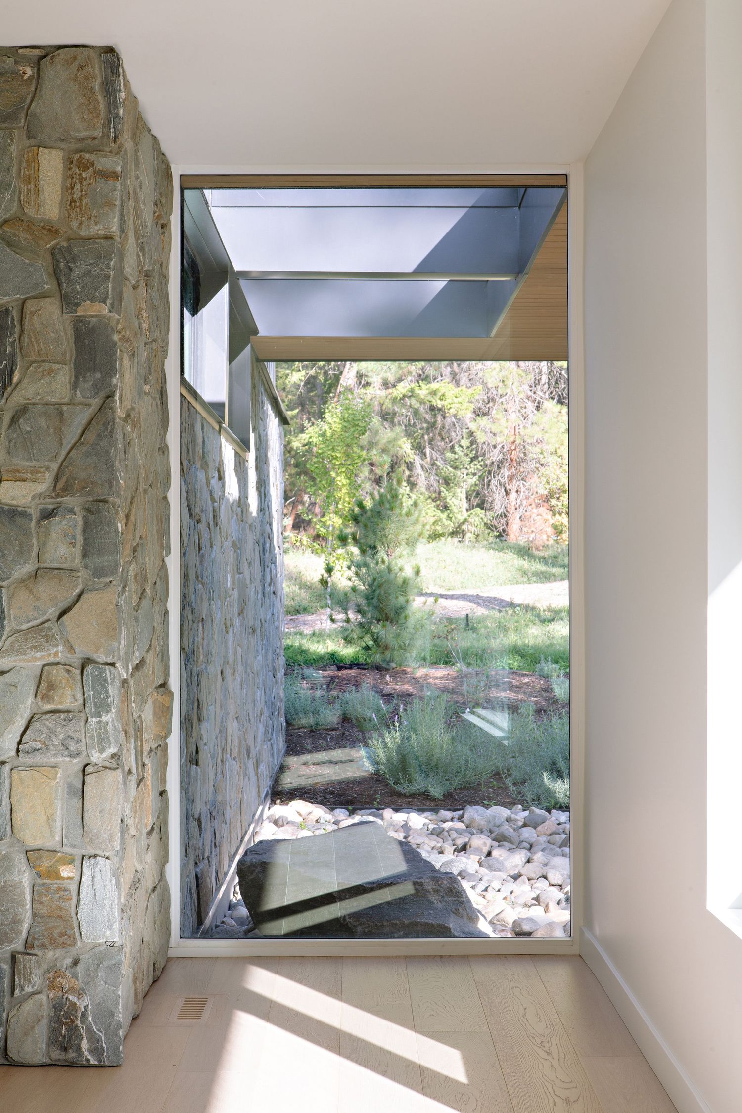 Modern architectural window framed by stone walls shows a tranquil garden view with natural lighting and rocky landscaping.