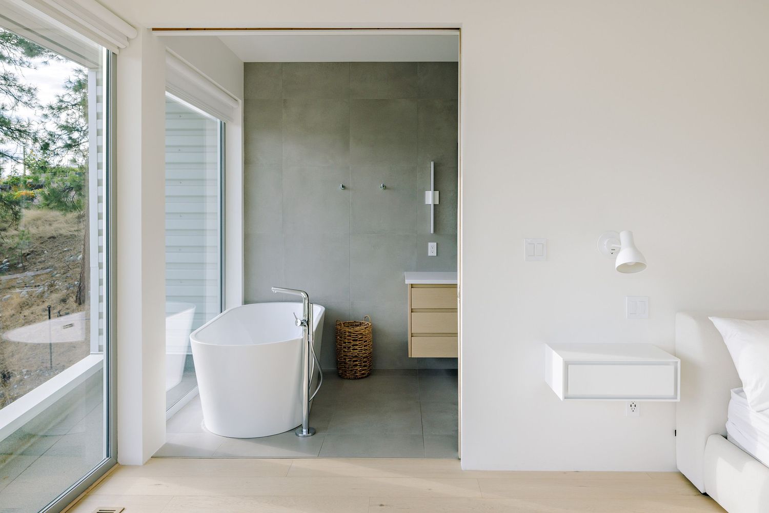 Modern bathroom interior featuring a freestanding white bathtub, large window, concrete floor and minimalist design elements.