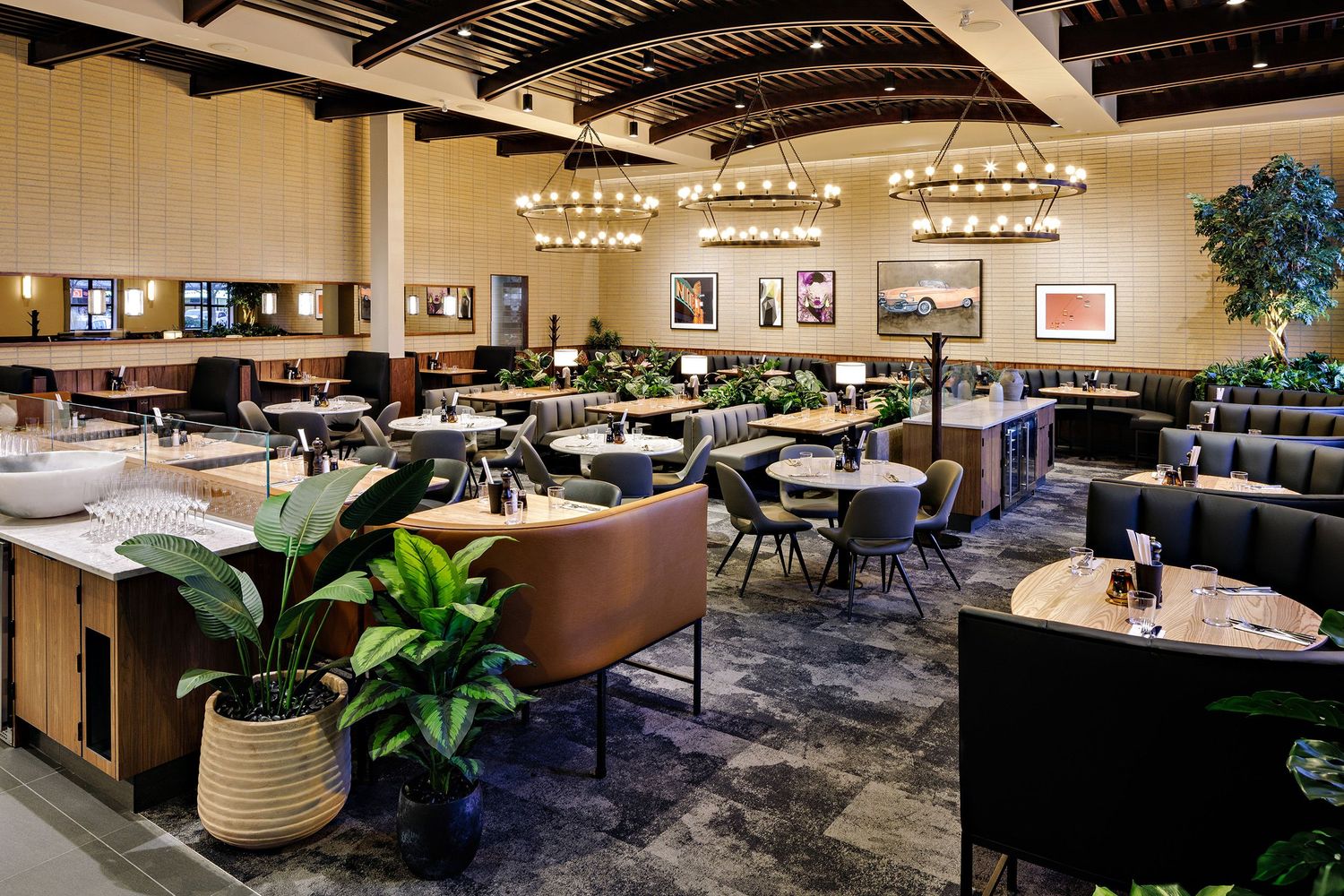 Elegant restaurant dining room with dark leather booths, round tables, and ornate chandeliers hanging from exposed beams.