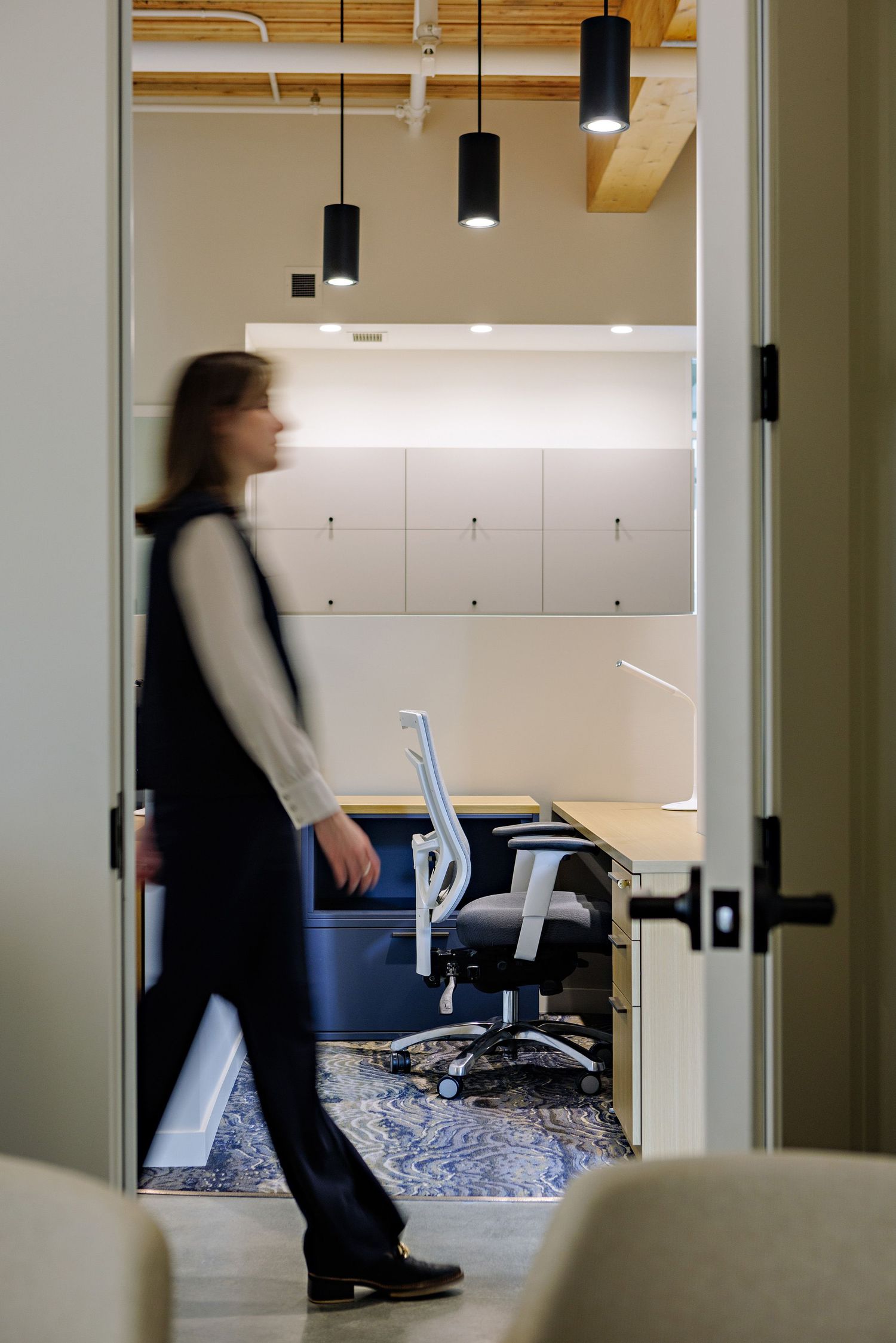 Motion-blurred figure walking through office doorway with pendant lights and office chairs visible.