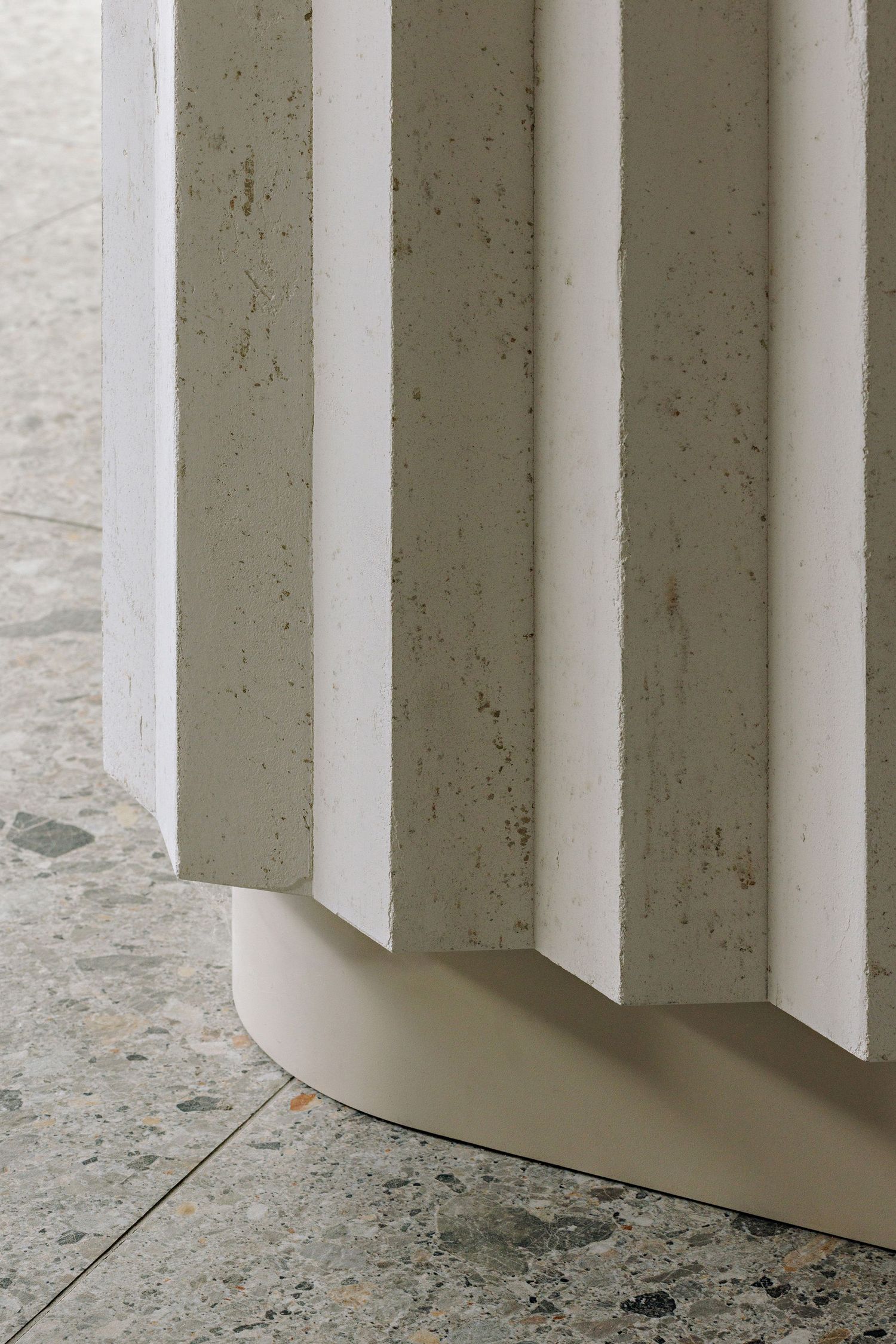 Close-up view of white curved architectural columns casting shadows on a textured stone floor.