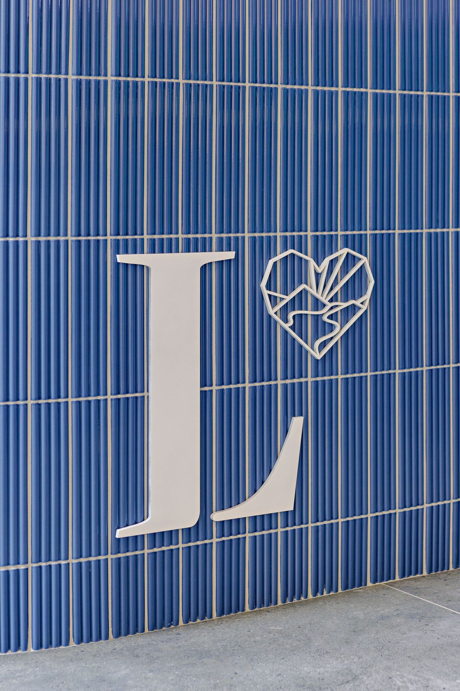 A large white letter L and geometric heart symbol mounted on a blue ribbed wall background.