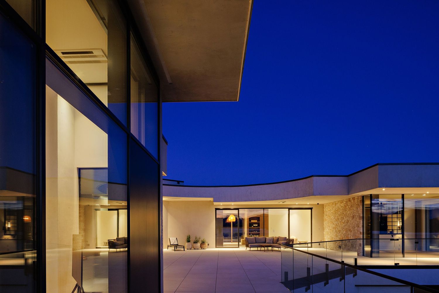 Modern luxury villa with glass walls illuminated at dusk against a deep blue sky.
