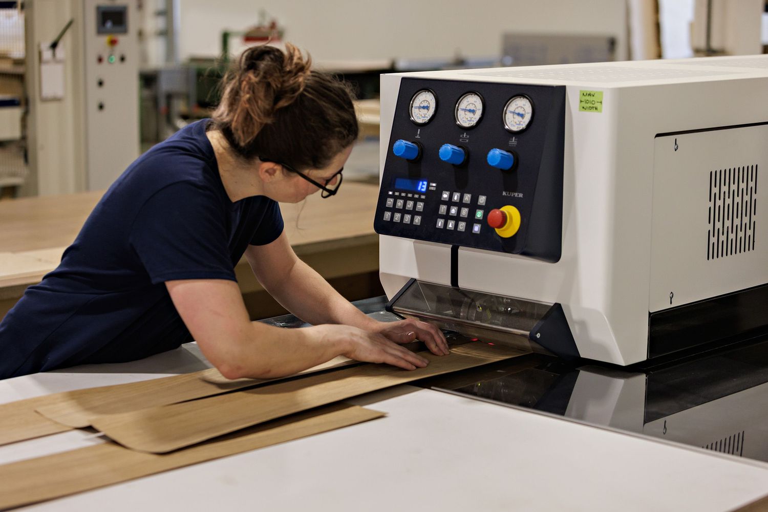 Worker operating industrial printing machine with digital controls in manufacturing facility.