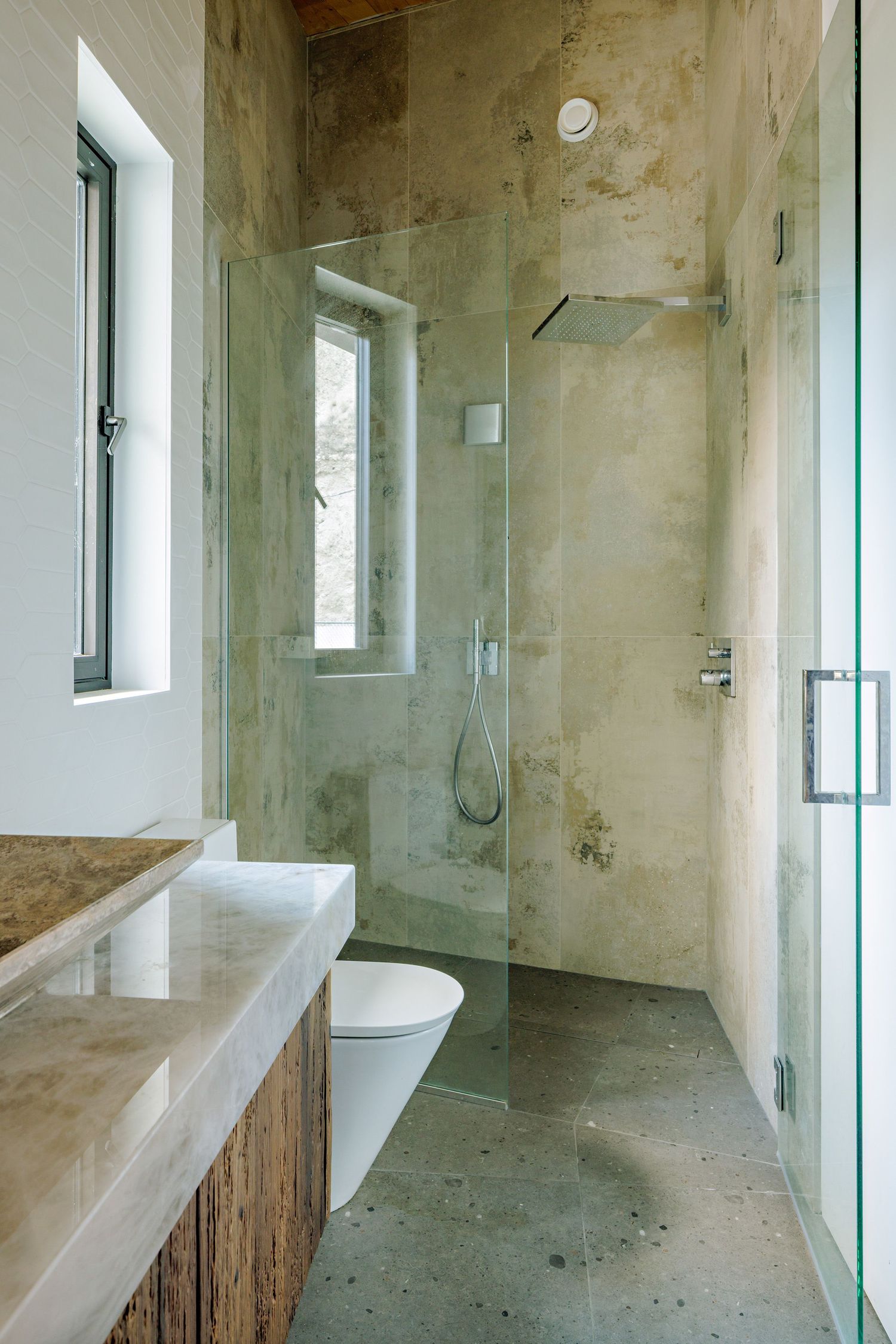 Modern bathroom interior with glass shower partition, concrete walls, and wooden shelf in minimalist design style.