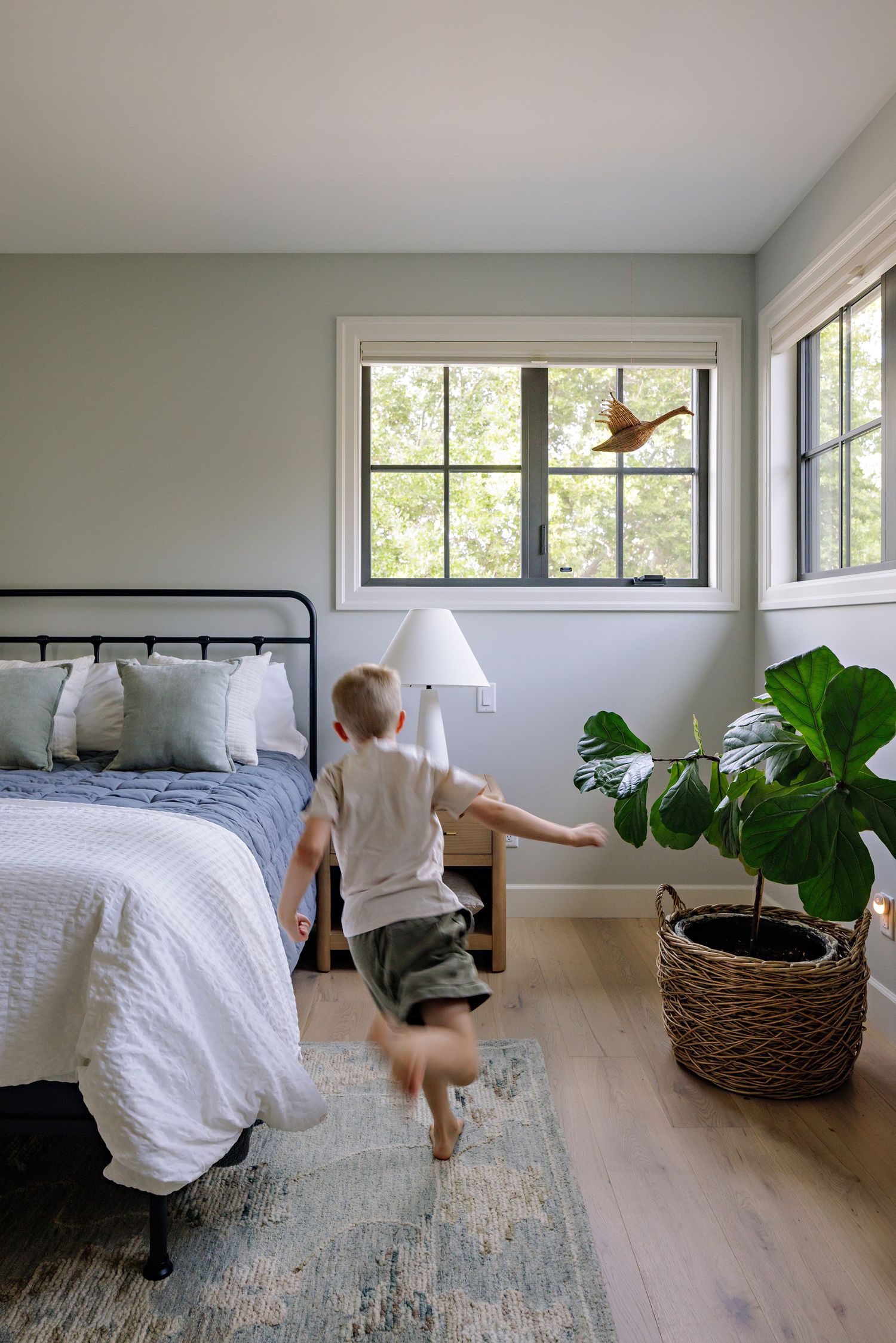 A series of photos showing someone making a bed with white linens in a bright modern bedroom with large windows and plants.