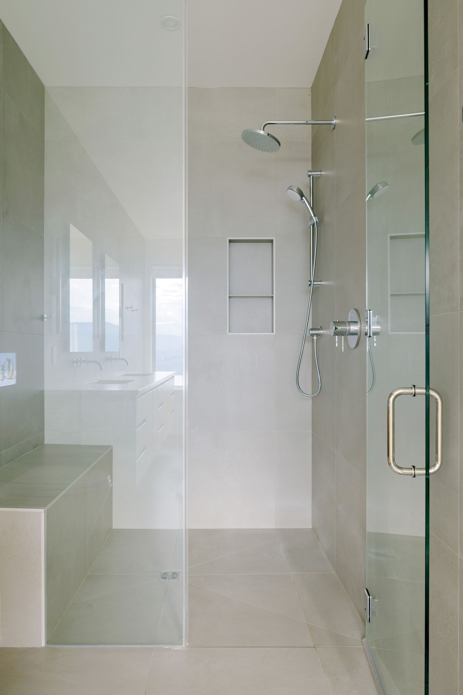 Modern walk-in shower featuring glass enclosure, chrome fixtures, built-in shelves and bench in minimalist neutral tones.