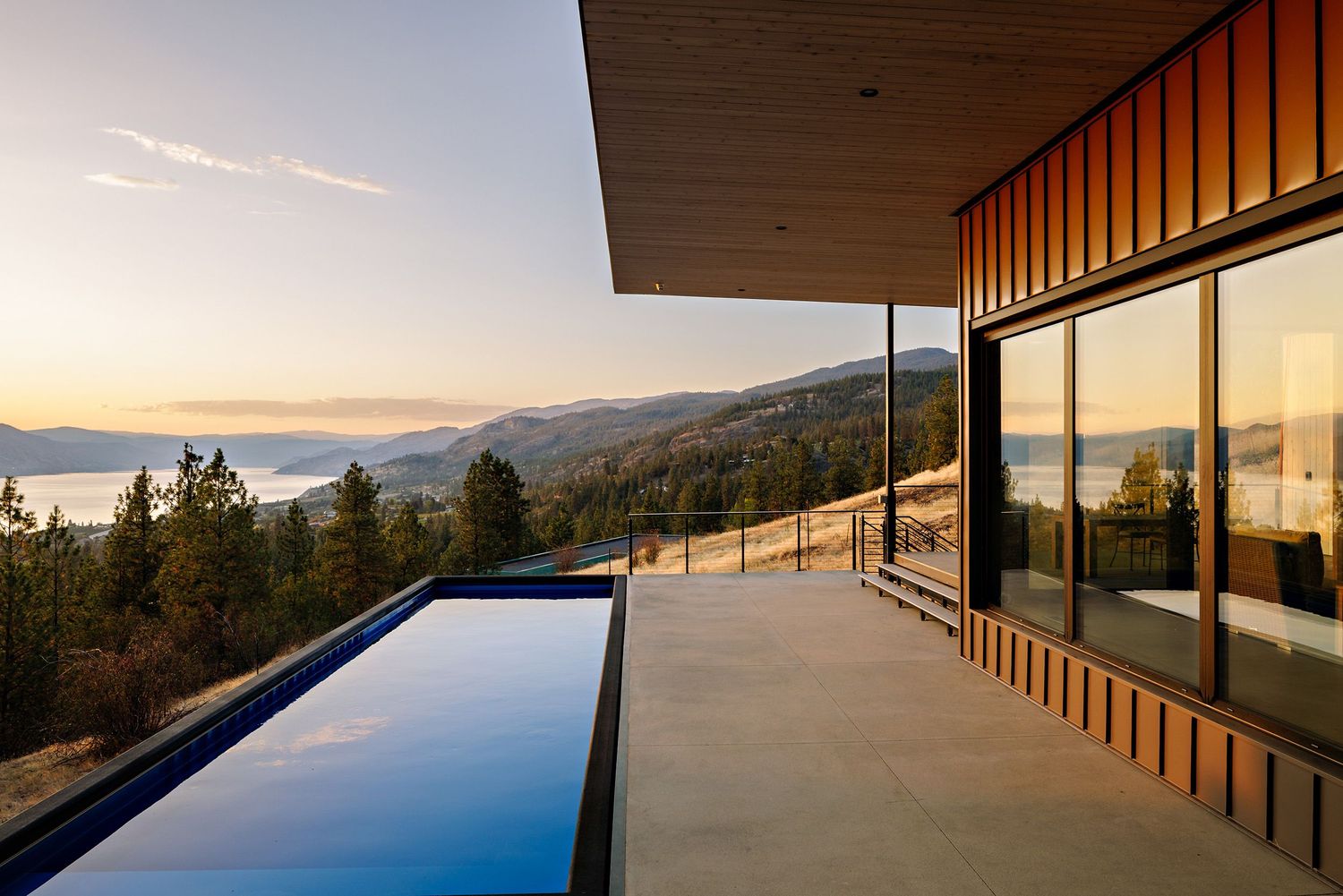 Luxurious infinity pool overlooking mountain landscape at sunset with modern architectural deck and glass walls.